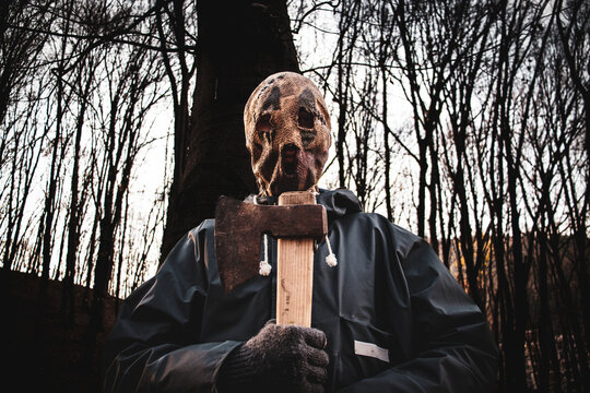 A person with a horror mask in the forest and an ax in his hand