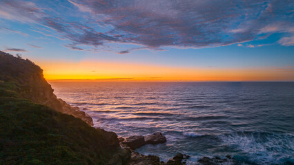Ocean sunrise panorama with headland and clouds