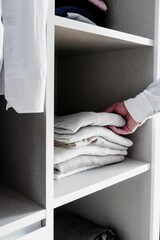 Person reaching into a closet to grab a stack of neatly folded clothes.