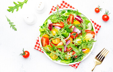 Fresh vegan vegetable salad with colorful tomatoes, cucumber, red onion, lettuce and arugula. White table background, top view