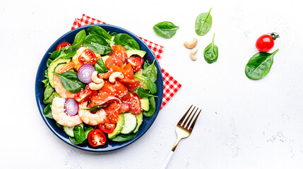 Fresh salad for keto diet with shrimp, salmon, avocado, spinach, cucumber, tomato, cashew nuts, sesame. Low-carbohydrate lunch rich in healthy fats. White table background, top view