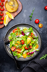 Summer vegan vegetable salad with colorful tomatoes, fresh cucumber, red onion, lettuce and arugula. Black table background, top view
