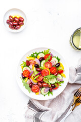Vegan salad with kalamata olives, cherry tomato, yellow paprika, cucumber and red onion, tasty and healthy mediterranean food, low calories eating. White table background, top view