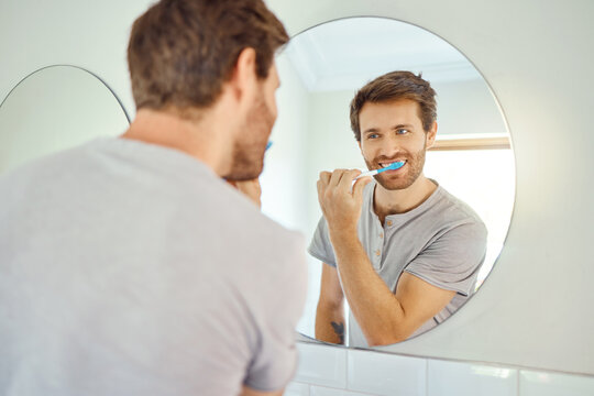 Brushing teeth, morning routine and mirror with man in bathroom for self care, oral hygiene and dental. Cleaning, smile and health with face of male person at home for beauty, wellness and reflection