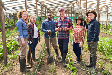 Smiling multiracial farmers standing with tools at greenhouse