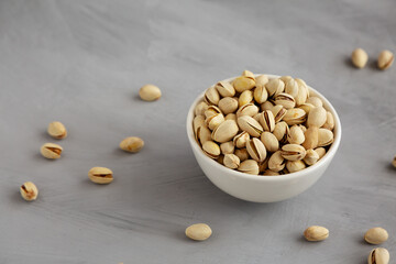 Salted and Roasted Pistachios in a Bowl on a gray background, side view.