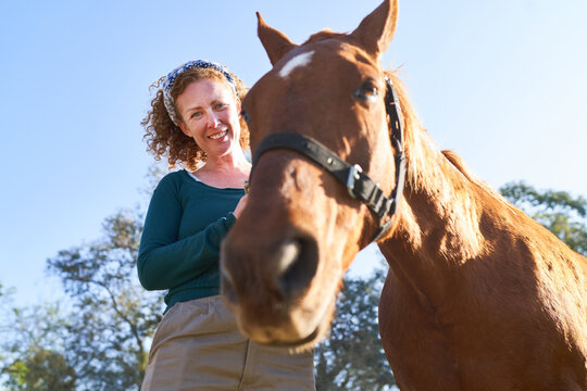 Low angle view of smiling female farmer with brown horse
