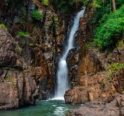 Stunning long-exposure of a majestic waterfall cascading down through a lush green forest © Kd32/Wirestock Creators