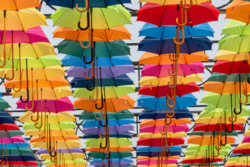 Fototapeta na wymiar Lots of umbrellas coloring the sky in the city,Colorful yellow red blue white green pink color fabric umbrella with blue sky cloud background