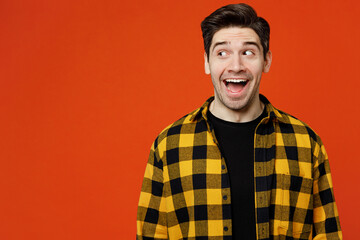 Young surprised happy amazed caucasian man he wear yellow checkered shirt black t-shirt look aside on workspace area mock up isolated on plain red orange background studio portrait. Lifestyle concept.