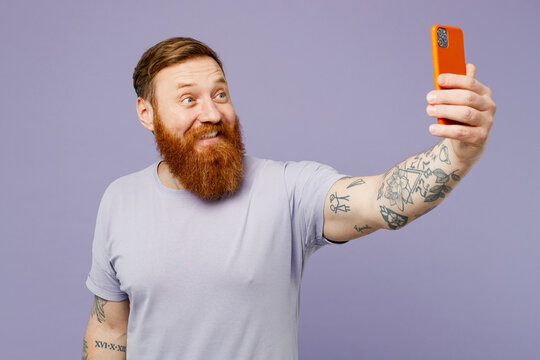 Young redhead bearded man he wear violet t-shirt casual clothes doing selfie shot on mobile cell phone post photo on social network isolated on plain pastel light purple background. Lifestyle concept.