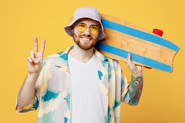 Young smilin happy fun cheerful man he wear blue shirt white t-shirt casual clothes hold in hand skateboard pennyboard show v-sign isolated on plain yellow background. Tattoo translates life is fight.