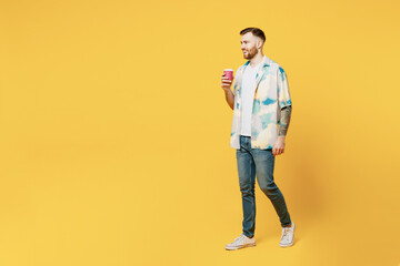 Full body side view young man he wear blue shirt white t-shirt casual clothes hold takeaway delivery craft paper brown cup coffee to go isolated on plain yellow background studio. Lifestyle concept.