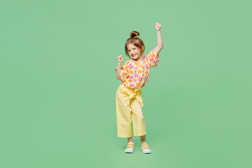 Full body little child kid girl 6-7 years old wears casual clothes doing winner gesture celebrate clench fists say yes isolated on plain green background. Mother's Day love family lifestyle concept. - obrazy, fototapety, plakaty