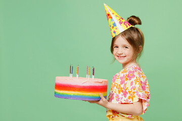 Little cute child kid girl 6-7 years old wear casual clothes birthday hat cone have fun hold cake isolated on plain pastel green background studio portrait. Mother's Day love family lifestyle concept.