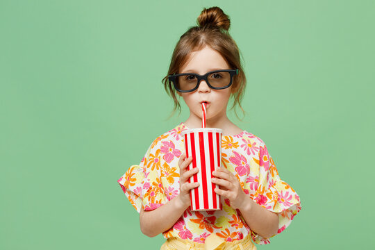 Young Fun Smiling Cheerful Satisfied Happy Child Kid Girl 6-7 Years Old In 3d Glasses Watch Movie Film Hold Cup Of Soda Pop In Cinema Looking Camera Isolated On Plain Green Background Studio Portrait.