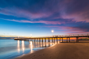 Fototapeta na wymiar Henley Beach jetty at dusk with the tranquil sea embracing the weathered pillars with purple cluds above, South Australia