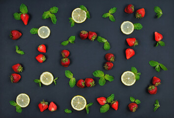 Fruit set from fresh strawberries, mint leaves and sliced lemon, isolated on black background .Round frame from strawberries and mint leaves at the center. Top view, flat lay .Free copy space