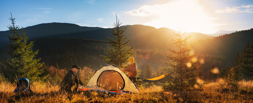 Two tourists pitch tent in the mountains at sunset. Family vacation in mountains. - Powered by Adobe