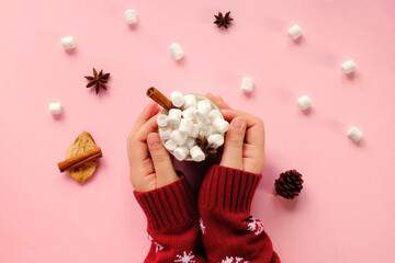 Winter drink, white mug with marshmallows in female hands in knitted Christmas Sweater on pink...