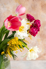 Glass vase with bouquet of beautiful tulips and mimosa in the light background