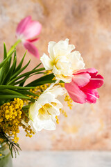 Glass vase with bouquet of beautiful tulips and mimosa in the light background
