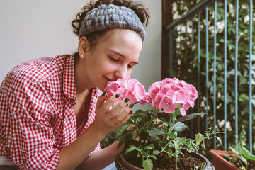 Young attractive woman caring for hydrangea in flowerpot on balcony