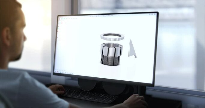 An engineer designs machine components on a computer using CAD software at a company manufacturing machines for the industry. A production hall, in the background