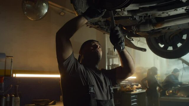 Middle Eastern auto mechanic working in garage standing under car repairing wheel using wrench tool