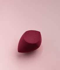 Red cosmetic sponge in the shape of an egg on a pink background