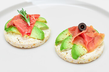 Rice Cake Sandwich with Avocado, Jamon, Olives and Rosemary on White Plate. Easy Breakfast. Quick and Healthy Sandwiches. Crispbread with Tasty Filling. Healthy Dietary Snack - Isolation