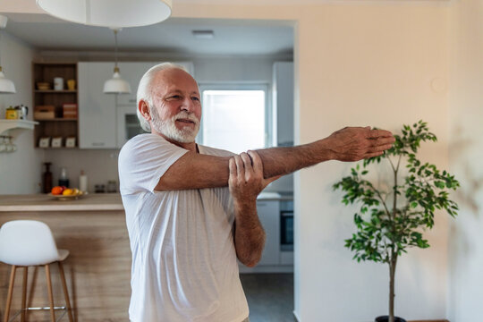 Portrait of a senior man stretching his arms at home. Health, exercise and yoga with senior man doing ground stretching before meditation and wellness workout.