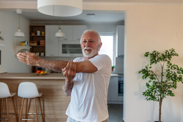 Portrait of a senior man stretching his arms at home. Health, exercise and yoga with senior man doing ground stretching before meditation and wellness workout.