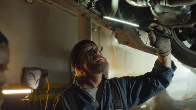 Two ethnically diverse mature and young auto mechanics working in car service garage finding breakageTwo ethnically diverse mature and young auto mechanics working in car service garage finding breaka