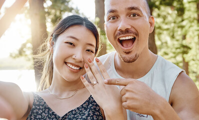 Couple, engagement and ring in selfie with smile, excited face and pointing for memory in forrest. Young man, happy woman and jewellery for proposal, marriage offer and photography for social network