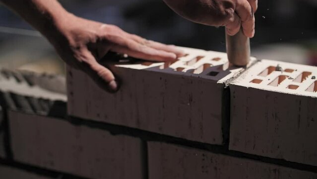 A builder lays bricks at a construction site, a close-up of the worker hands.