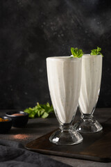 Two Indian Salty lassi with mint leaves and kala namak on black background. Healthy freshness lassi made of yogurt, water, spices and ice. Vertical format. Close up.
