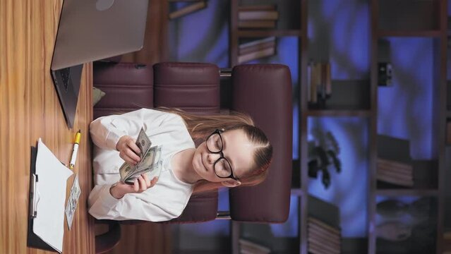 Delightful Little Girl Counting Money Received For Excellent Performed Work In Luxury Cozy Office. Vertical Video Of Happy Child Dressed In White Shirt And Big Black Glasses Hugging Us Dollars.