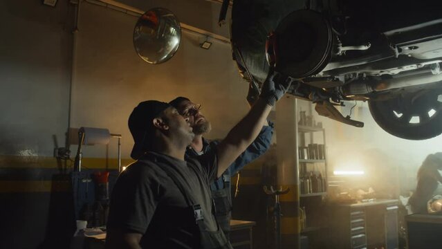 Mature Caucasian and young Middle Eastern auto technicians working in car repair shop finding breakage
