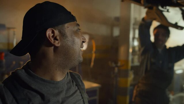 Selective focus of cheerful Middle Eastern auto mechanic repairing car wheel then doing high five with his Caucasian co-worker