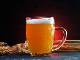 a mug of unfiltered wheat beer on a dark background. red backlight, wheat ears