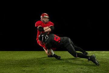 Fototapeta na wymiar Competitive spirit. Two men, american football players in full uniform and equipment on field playing over black background. Professional sport, action, lifestyle, match, hobby, training, ad concept