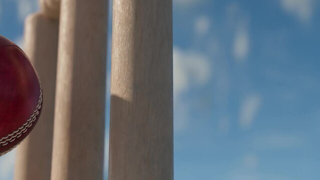 A slow motion close up of a red leather stitched cricket ball hitting wooden wickets