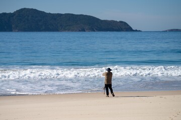 man fishing on the beach at dusk in queensland australia. casting a fishing line in from the beach