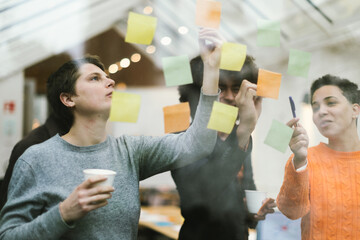 teamwork, young entrepreneurs make up their mind by working with adhesive notes attached to the...
