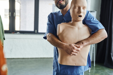 first aid training seminar, partial view of bearded medical instructor in uniform practicing...
