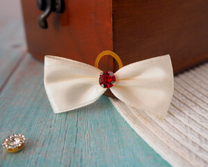 next to the wooden box is a small beige bow with a shiny red stone in the middle.  accessories. ...