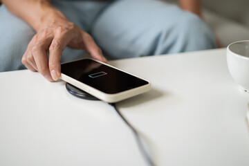 Charging mobile phone battery with wireless charging device in the table. Smartphone charging on a charging pad. Mobile phone near wireless charger Modern lifestyle technology concept.