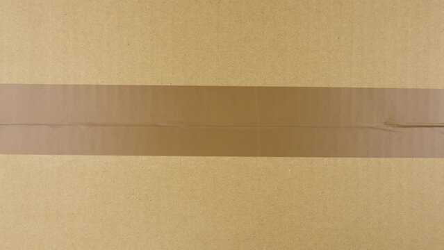 Hands sealing cardboard box with duct tape. View from top