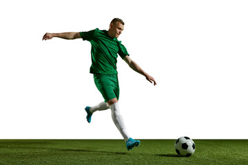 Young man in green uniform, football in motion, playing, kicking ball on sports field against white background. Concept of professional sport, action, lifestyle, competition, hobby, training, ad